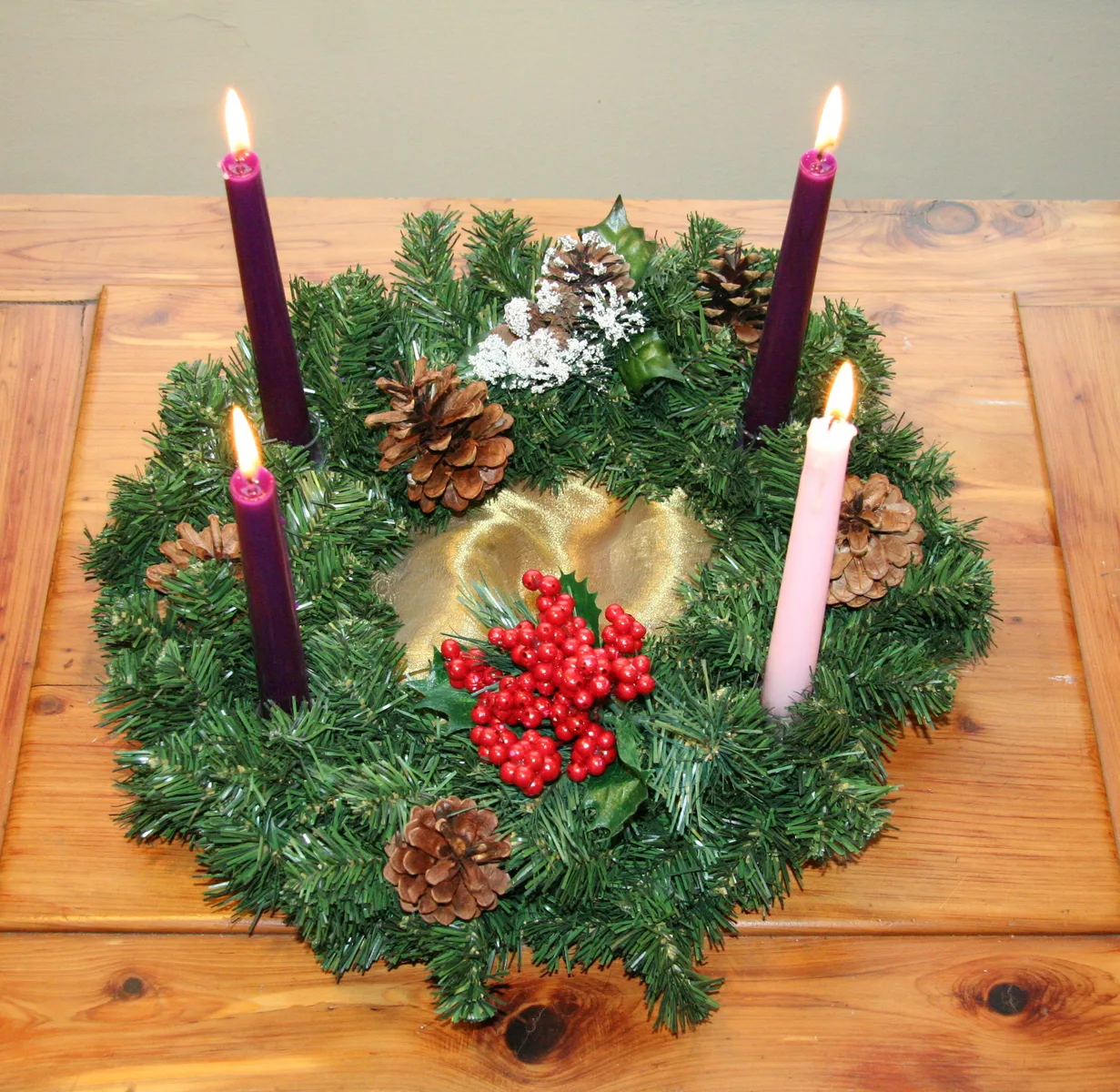 Adventskrans met brandende kaarsen, dennenappels en bessen