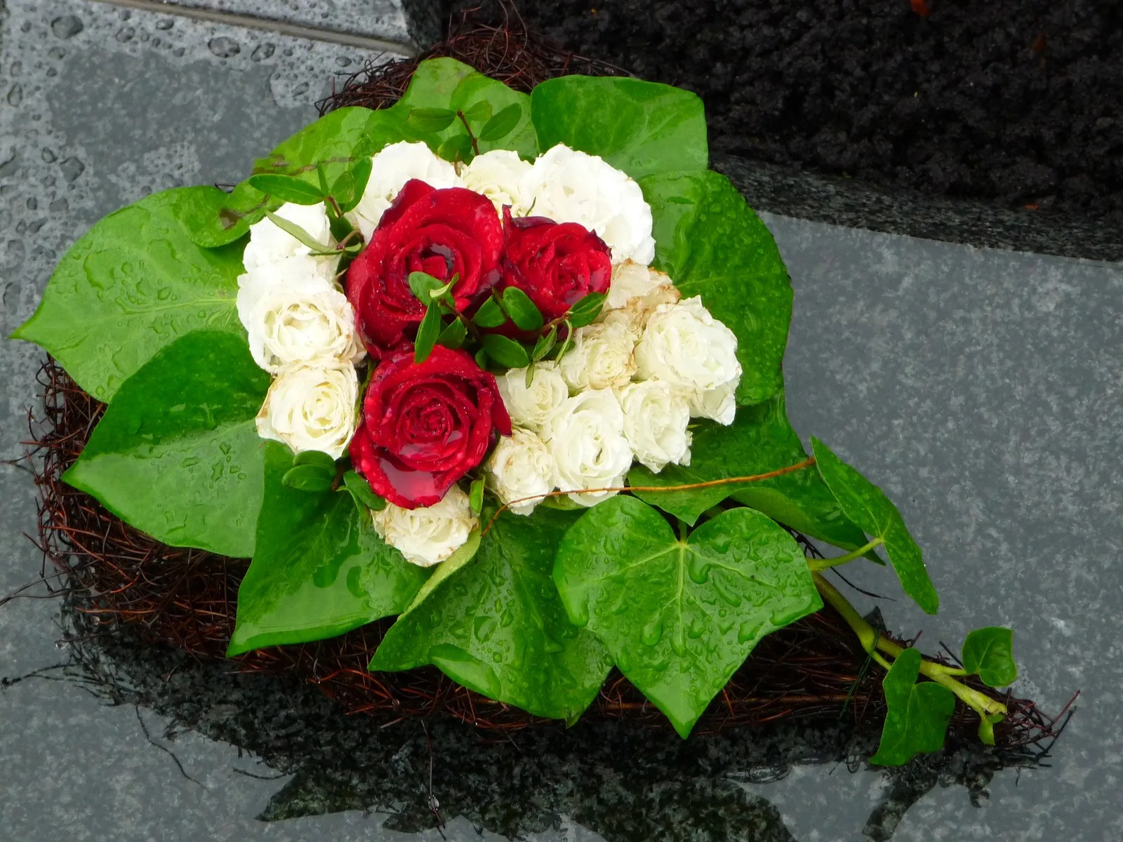 Sober rouwstuk met witte en rode bloemen op steen